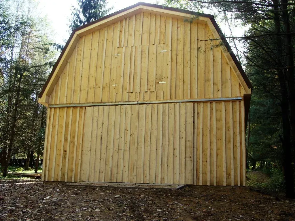 Wooden barn with vertical siding and dark roof, set among trees.