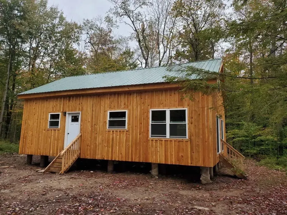 Wooden cabin with green roof and small steps in a wooded area.