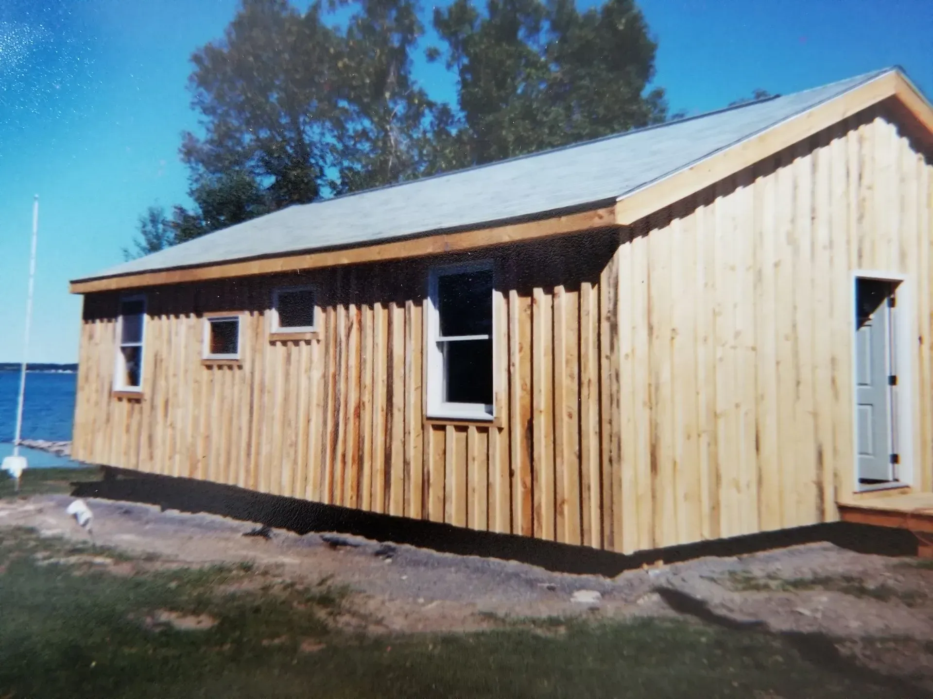 Wooden cabin with windows and door, set against a blue sky and water.