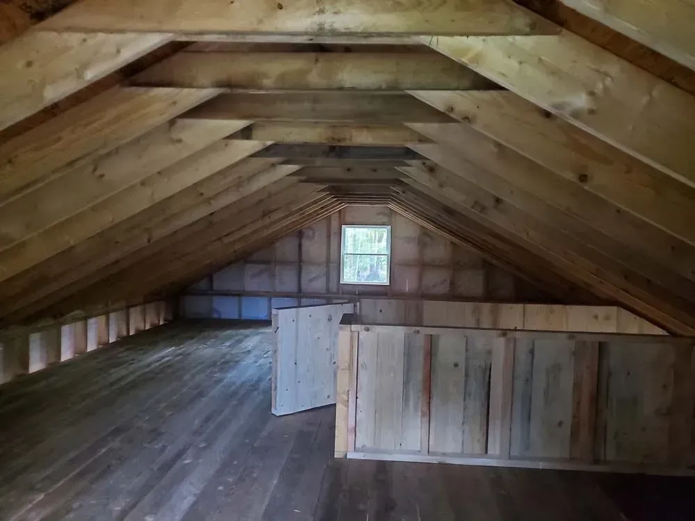 Wooden attic interior with rafters, small window, and low walls.