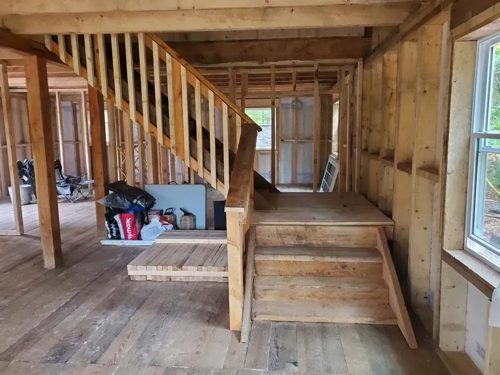 Interior of a wood-framed building under construction; a staircase with handrails and a landing.