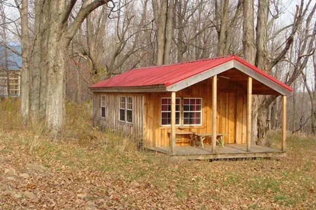 Small wooden cabin with red roof in a wooded area.