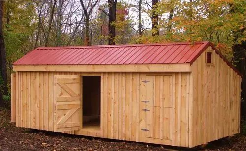 Wooden shed with red roof and open door in a wooded area.