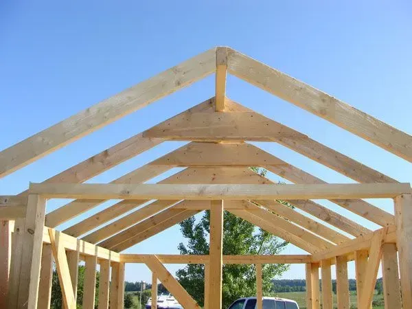 Wooden frame of a building under construction with angled roof beams against a blue sky.