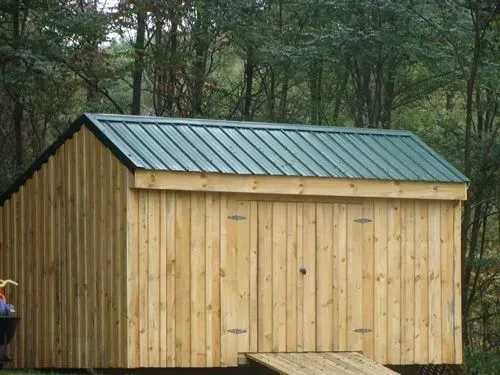 Wooden shed with green metal roof in a wooded area.