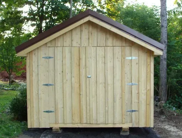 Wooden shed with brown roof and vertical wooden siding, in a grassy setting.