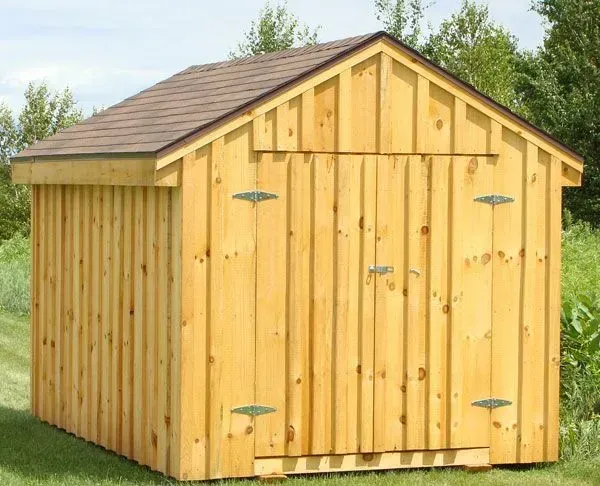 Wooden shed with brown roof in a grassy field.