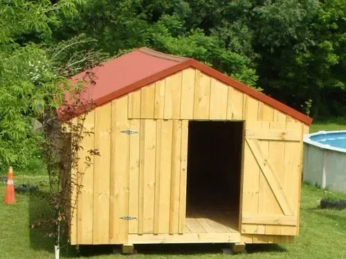 Wooden shed with red roof and open doorway, set on a grassy lawn.