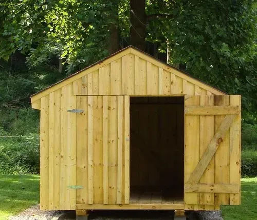 Wooden shed with open door, set in a grassy area near trees.