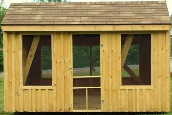 Wooden shed with brown roof, two windows with diagonal supports, and screened door.