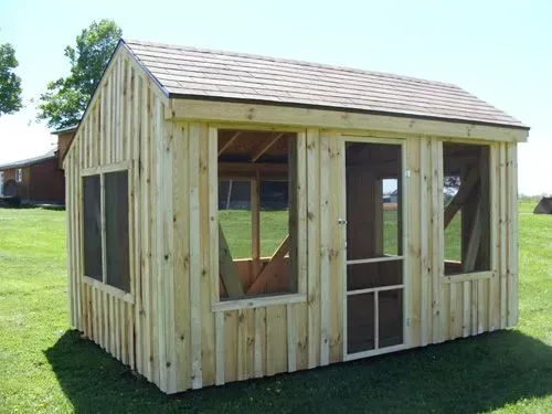 Wooden shed with a screened-in porch on green grass, under a blue sky.