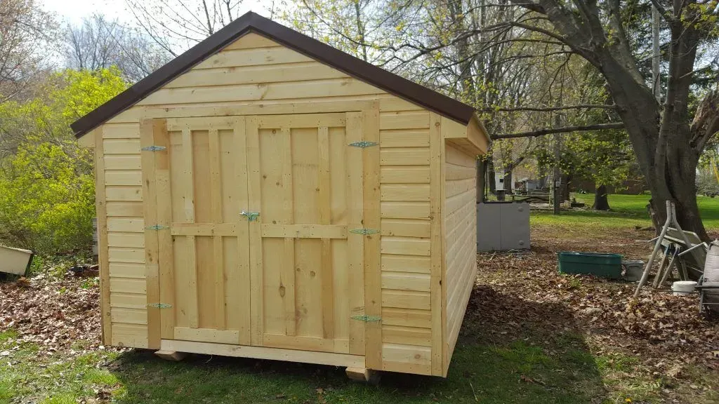 Wooden shed with double doors on a grassy lawn, brown roof, natural wood color.