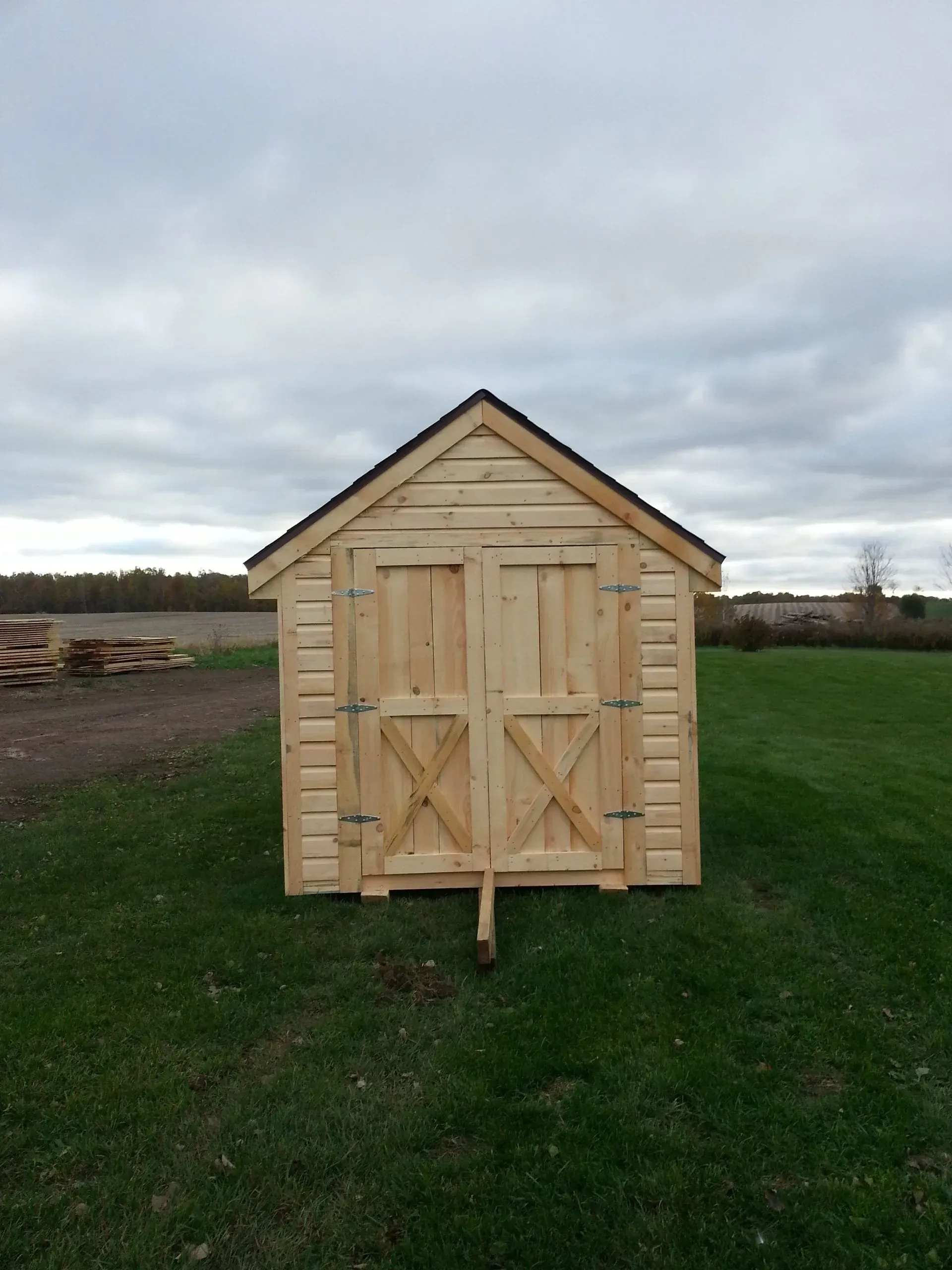 Wooden shed with double doors on a green lawn under a cloudy sky.
