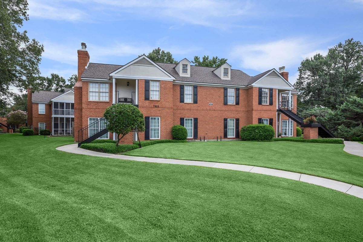 Large red brick house with green lawn and blue sky.