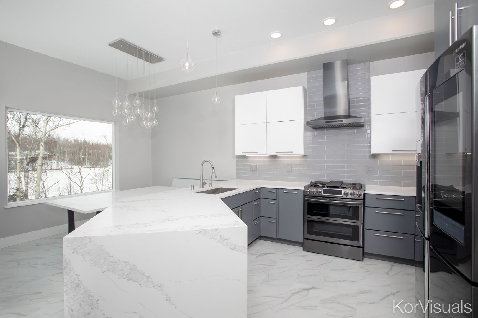 Modern white kitchen with marble island, gray cabinets, black appliances, and large window