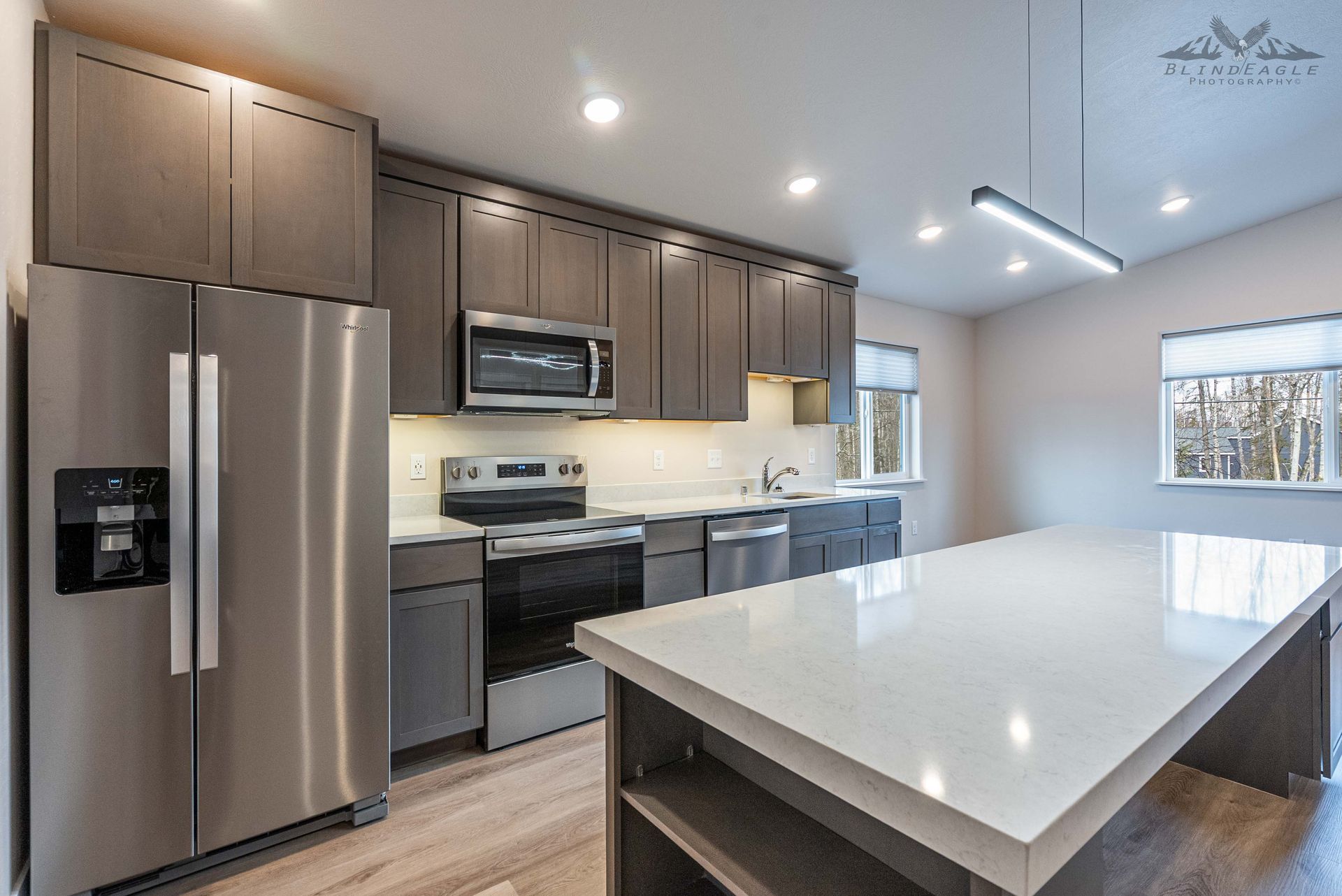 Modern kitchen with gray cabinets, stainless steel appliances, a large quartz-topped island, and light wood flooring.
