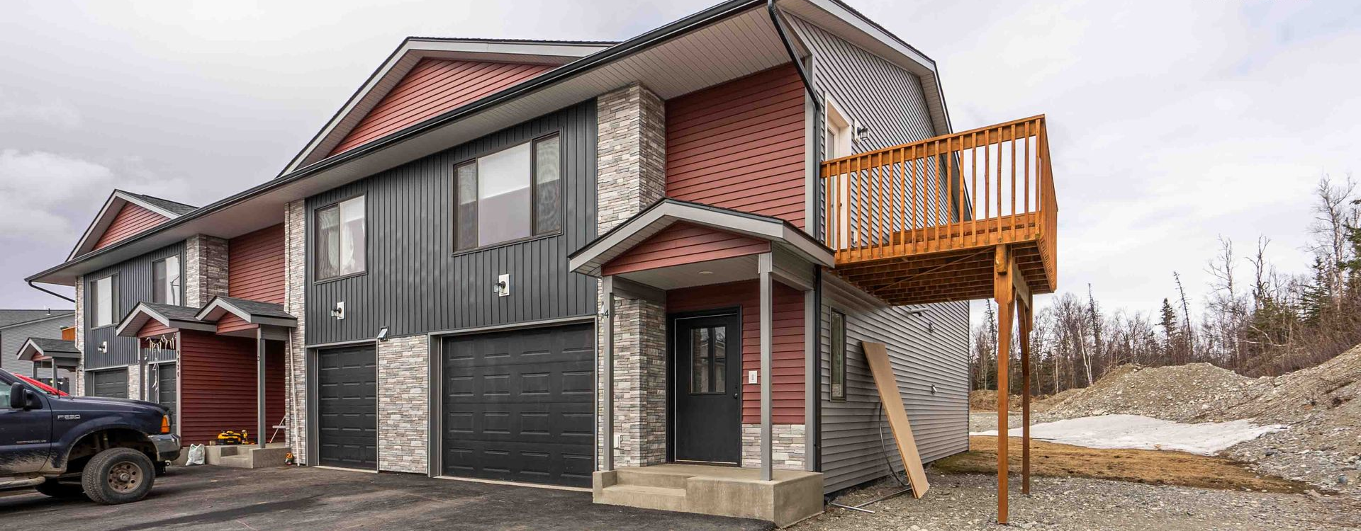 Modern gray house with red trim, attached garage, and wooden balcony on a snowy lot