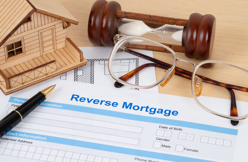 A reverse mortgage form with a wooden house , glasses , a pen and an hourglass.