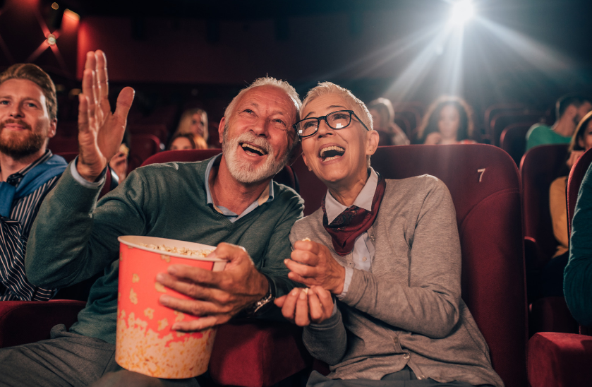 A couple of elderly people are sitting in a movie theater eating popcorn.