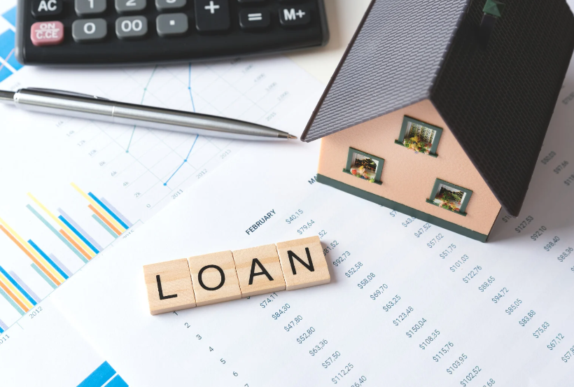 The word loan is written on wooden tiles next to a model house and a calculator.