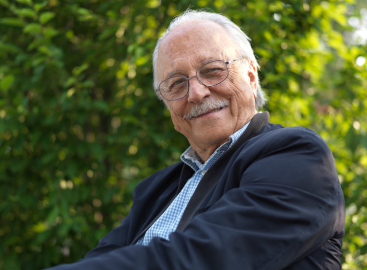 An older man wearing glasses and a suit is smiling for the camera