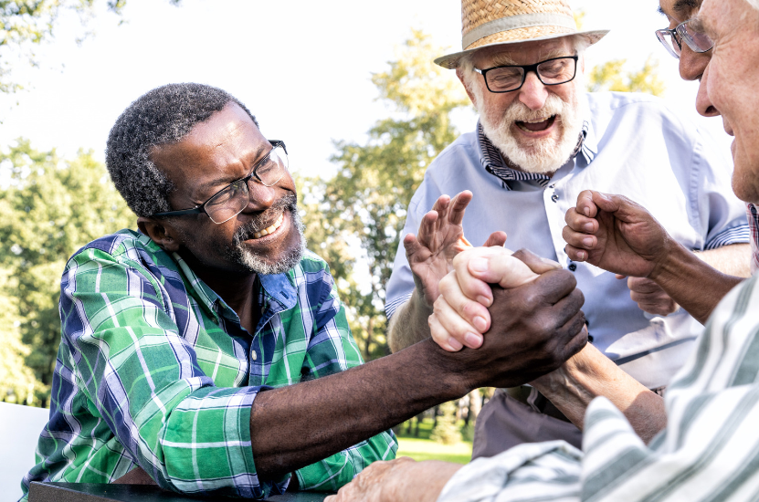 A group of older men are sitting at a table shaking hands.