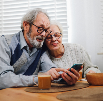 An elderly couple is sitting at a table looking at a cell phone.