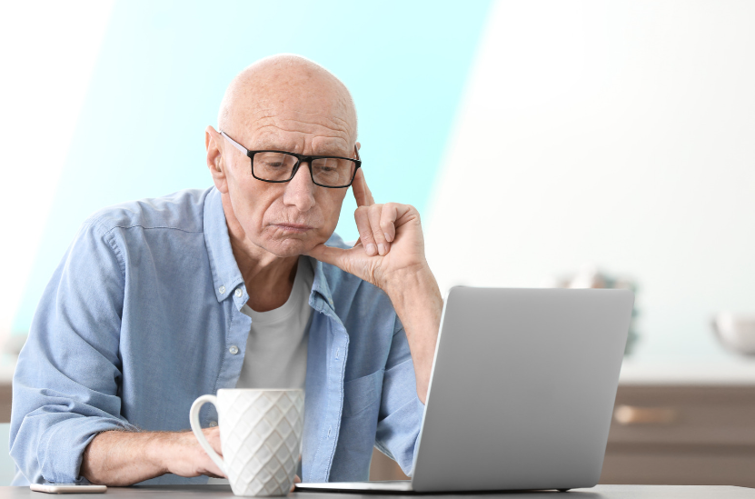An elderly man is sitting at a table using a laptop computer.