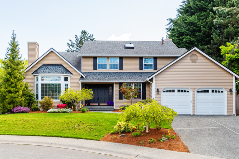 A large house with two garage doors and a lush green lawn
