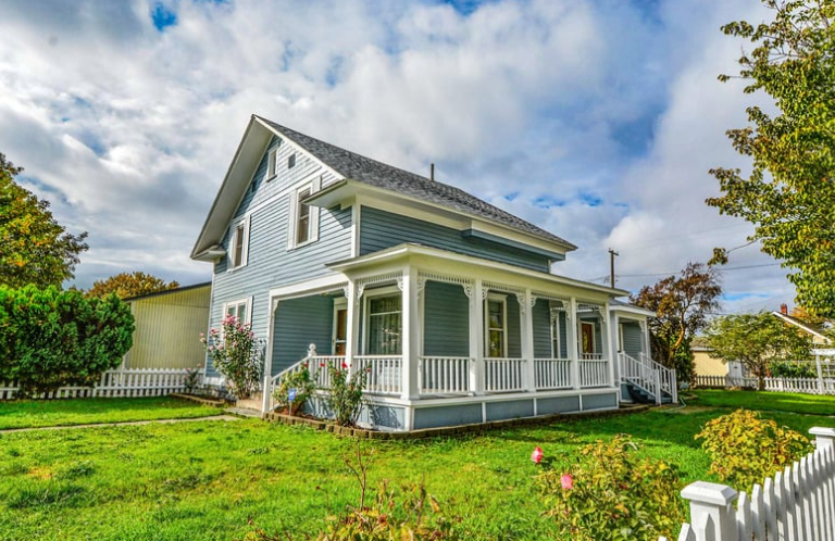 A blue house with a white porch and a white fence in front of it.