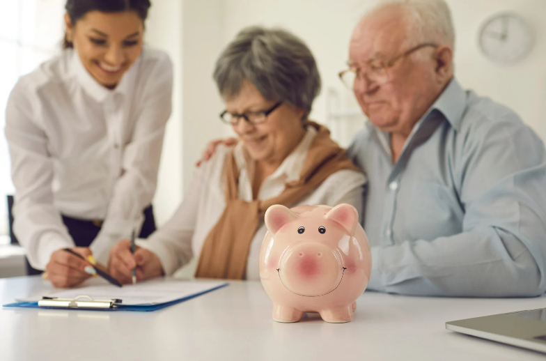 An elderly couple is sitting at a table with a piggy bank.