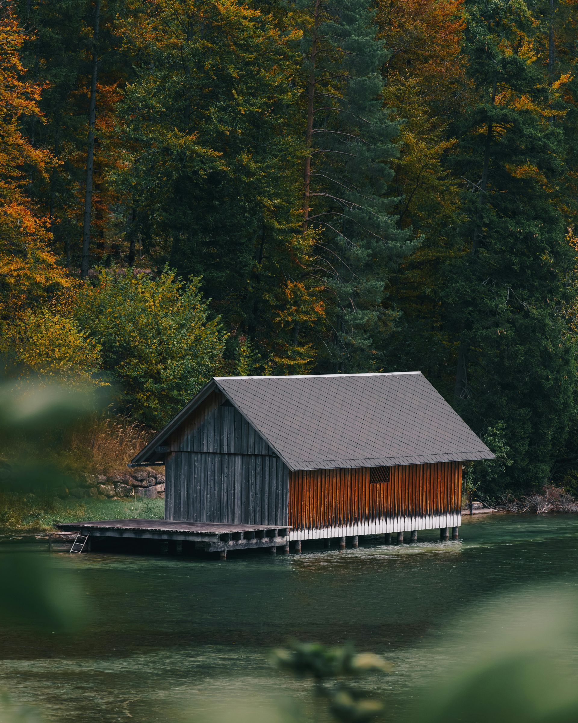 A small wooden house is sitting on a dock in the middle of a lake surrounded by trees.
