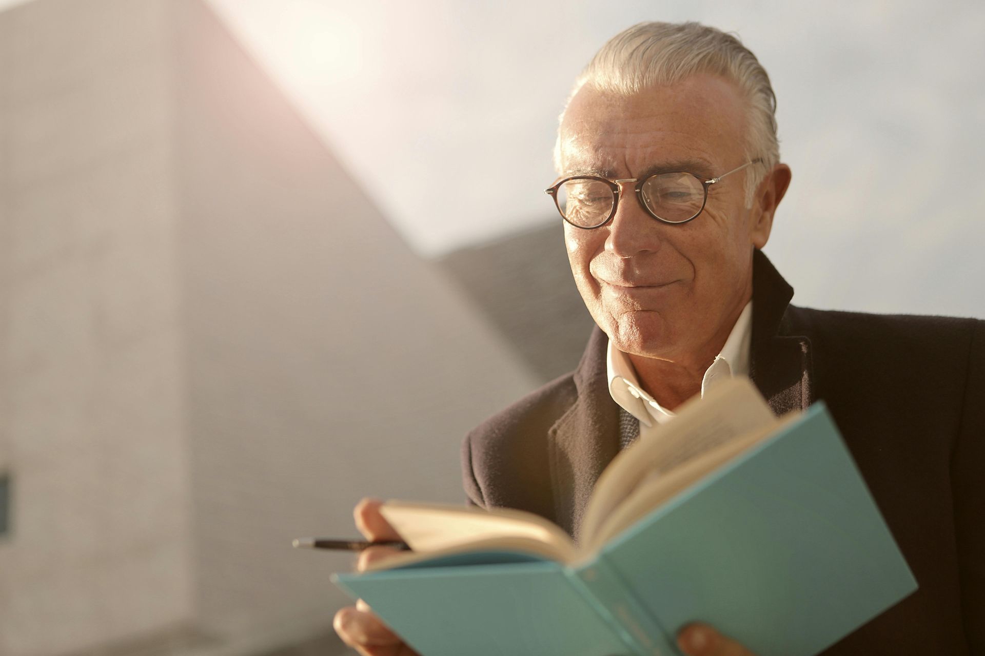 An older man wearing glasses is reading a book.