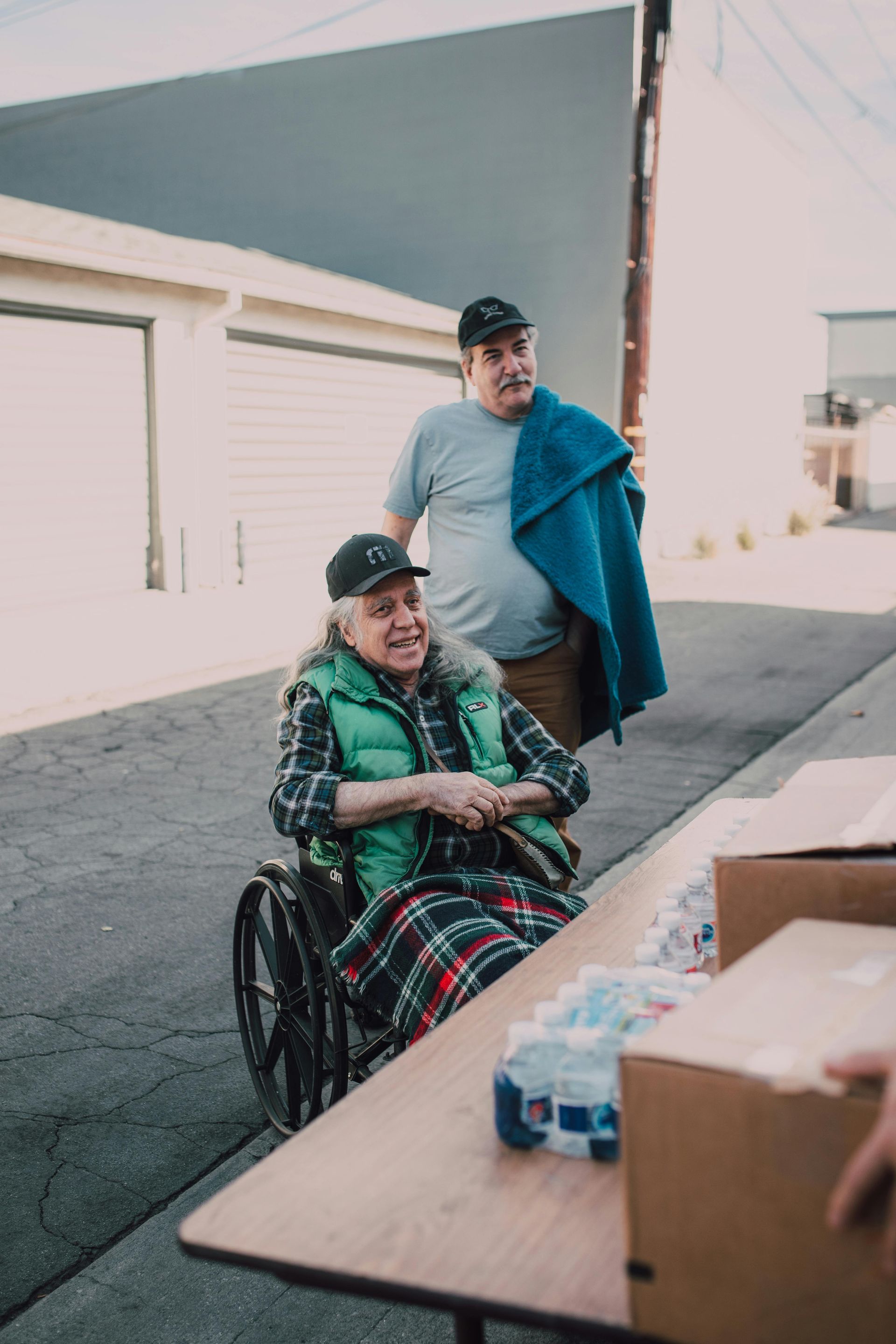 A man is standing next to an elderly man in a wheelchair.