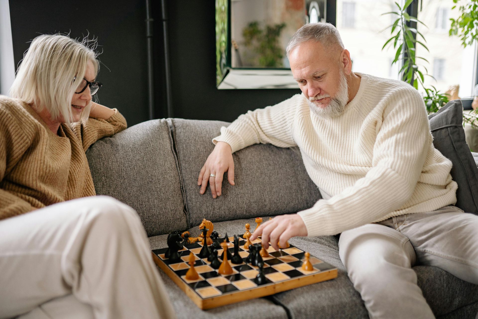 A man and a woman are sitting on a couch playing chess.