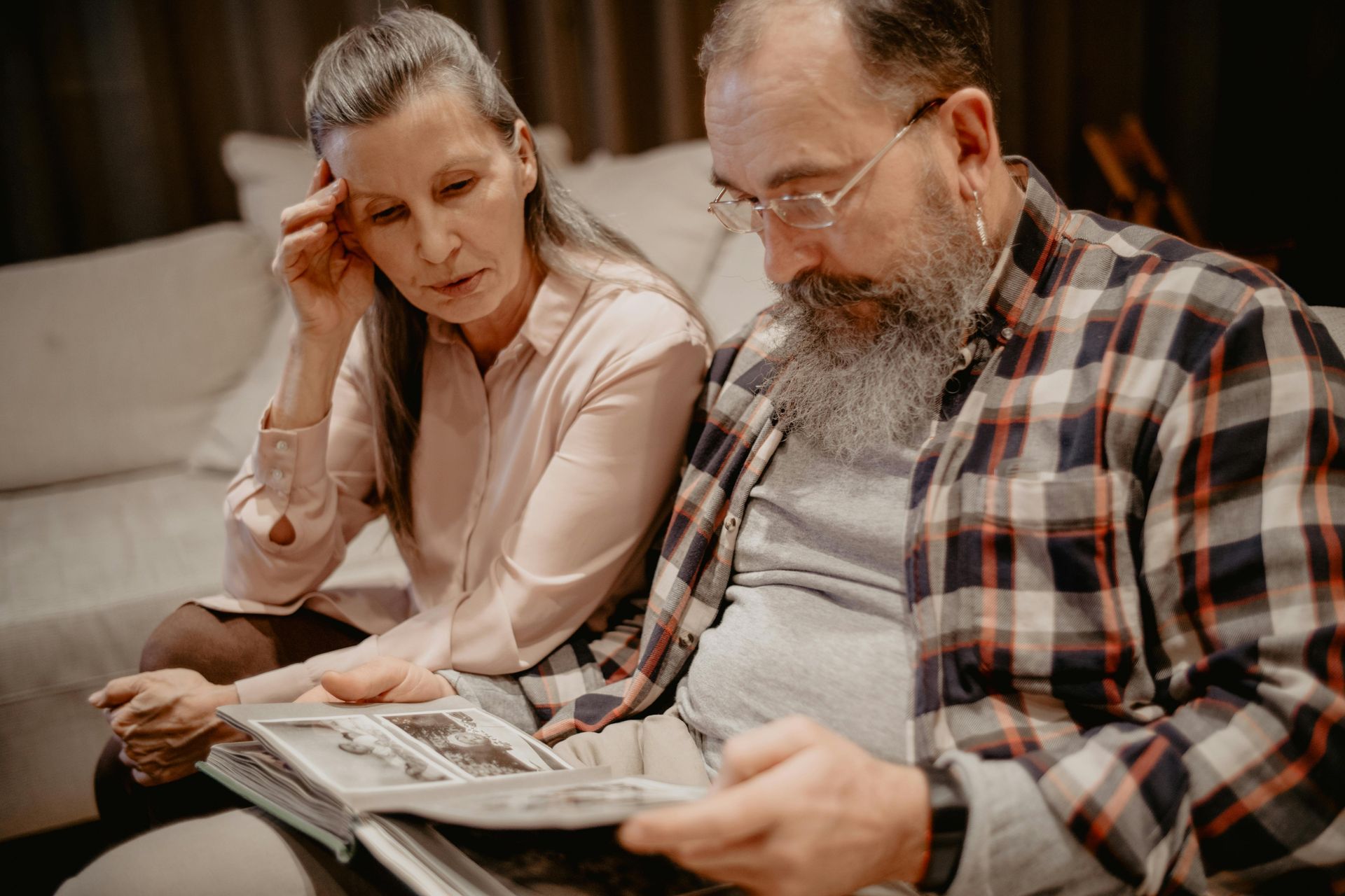 A man and a woman are sitting on a couch reading a newspaper.