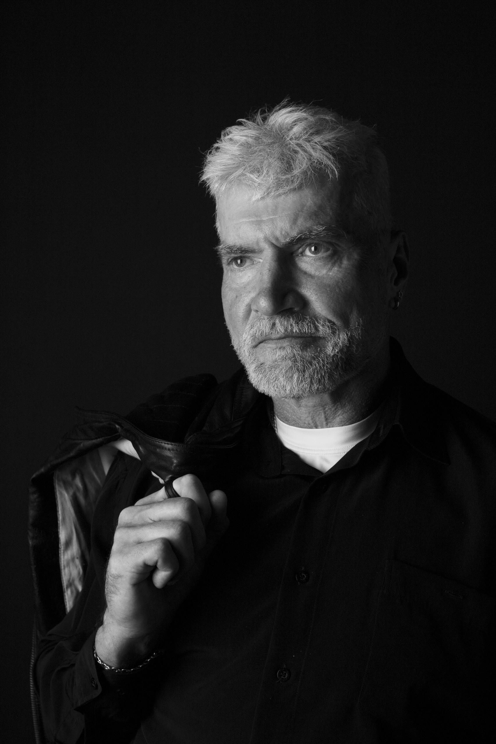 A black and white photo of a man with a beard wearing a black shirt.