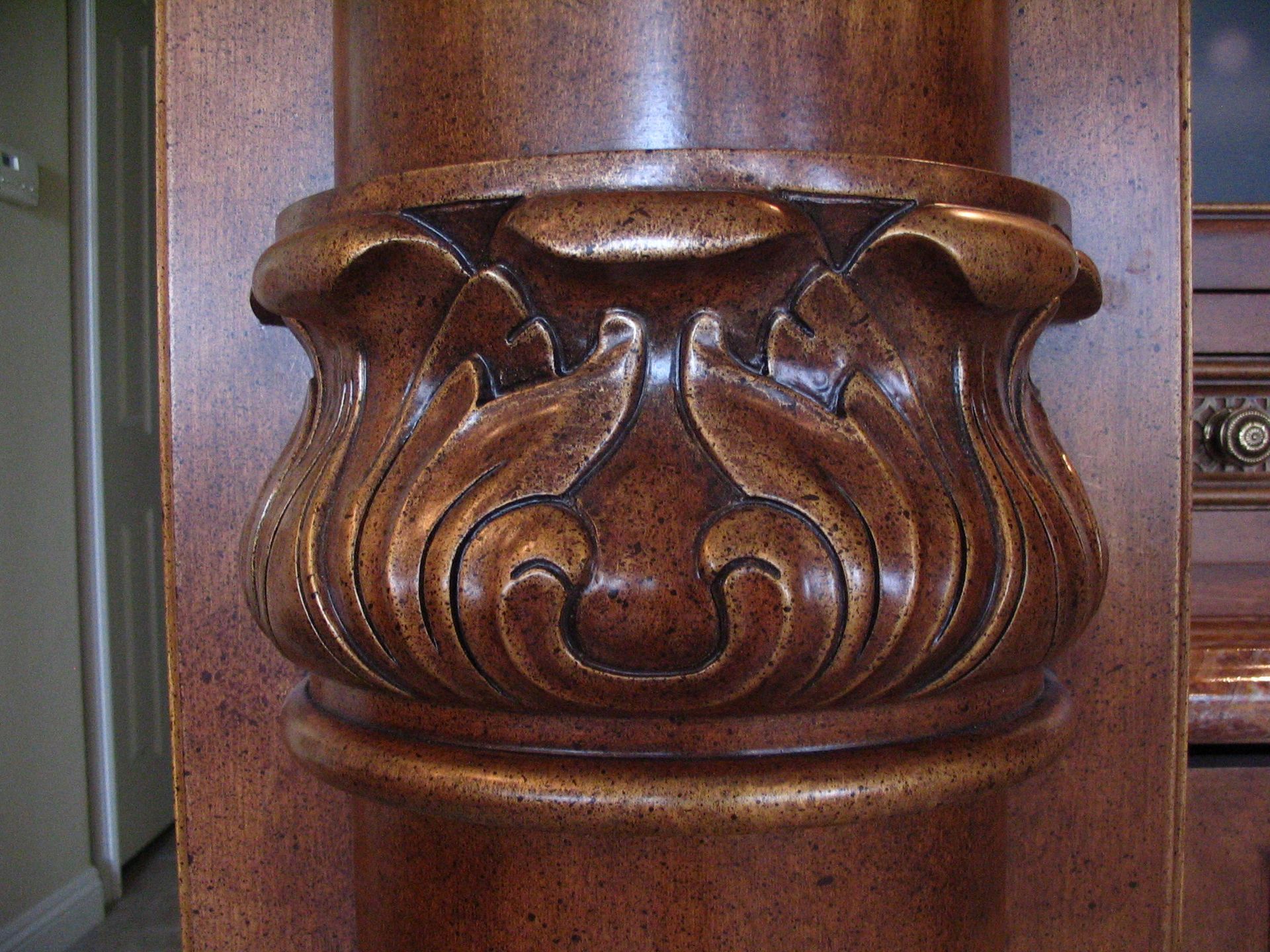 Wooden furniture detail with carved floral design and a column.