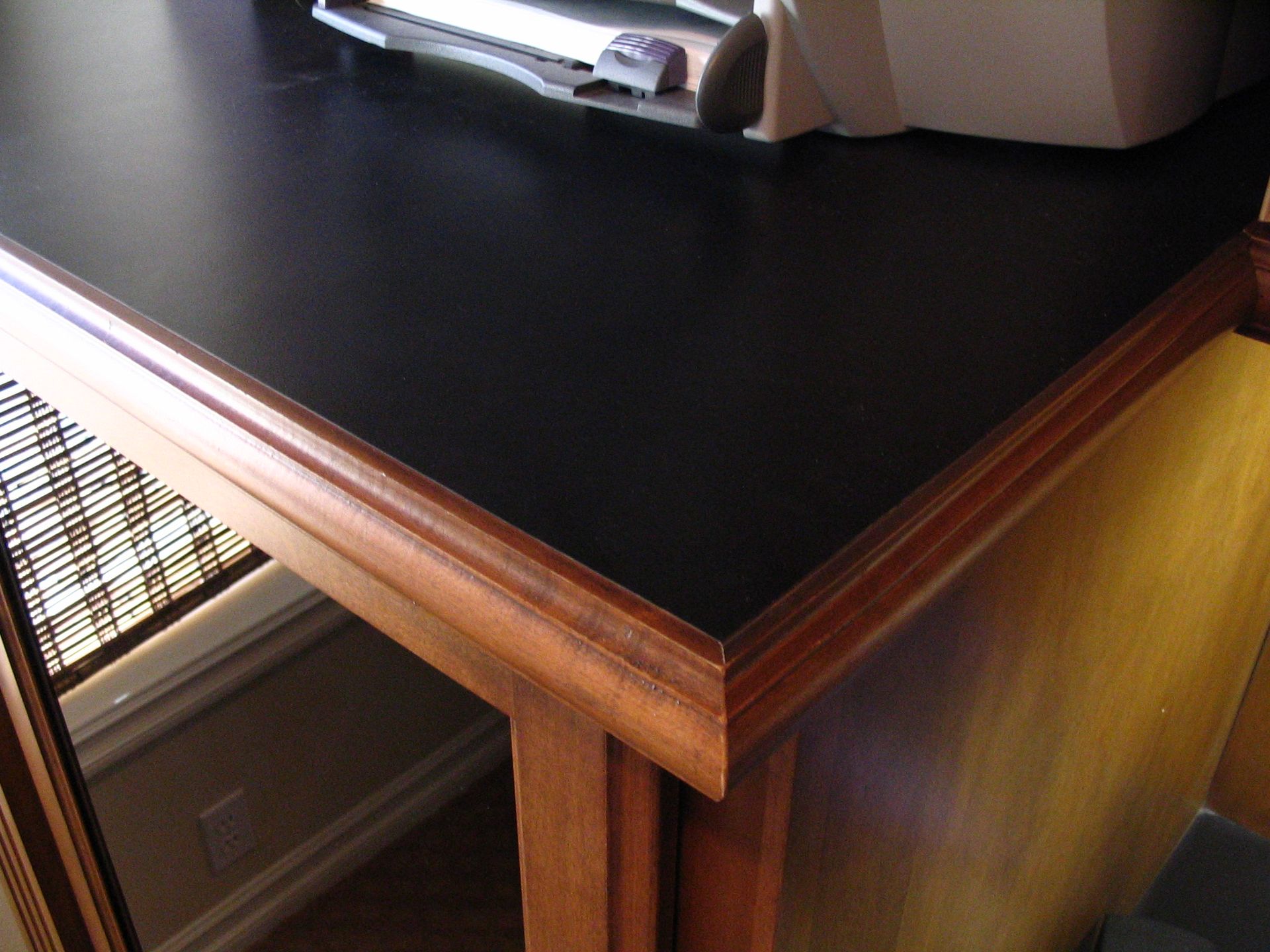 Black desktop with wooden trim, part of a desk, near a window.