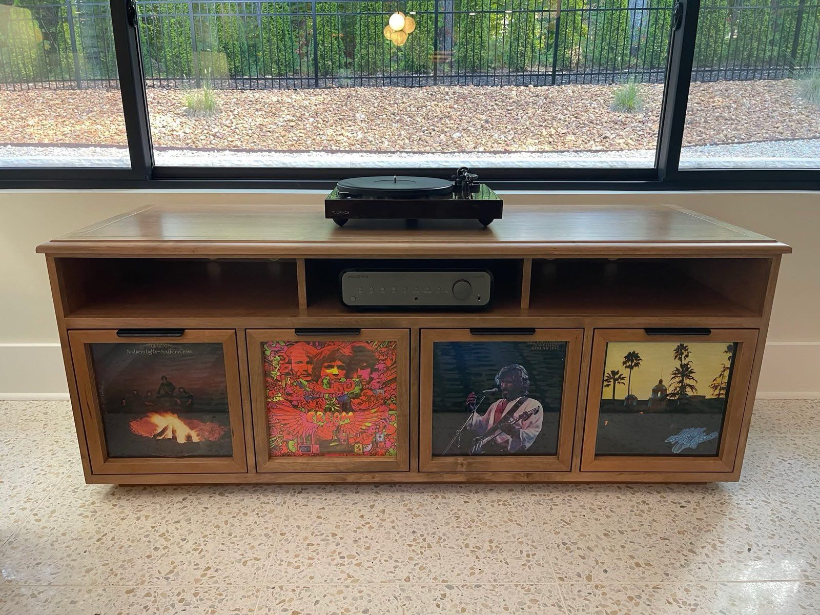 Wooden media console with vinyl record storage, turntable, and stereo components. Albums displayed behind glass doors.