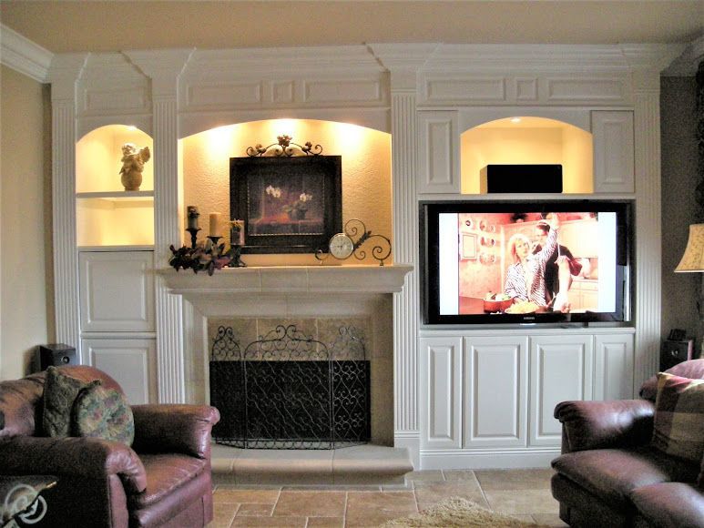 Living room with fireplace, built-in shelves, two leather chairs, and large TV mounted above the cabinet.