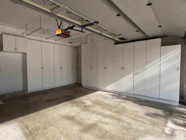 White storage cabinets line the walls of a garage with a concrete floor.