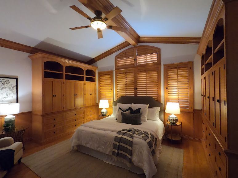 Bedroom with built-in wooden cabinets, bed with lamps, and wooden shutters. Ceiling fan hangs above.