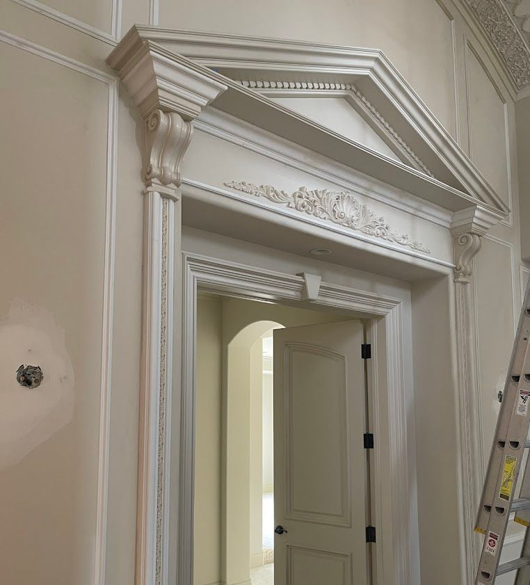 Ornate doorway with decorative trim, painted white. A partially opened door leads to a hallway.