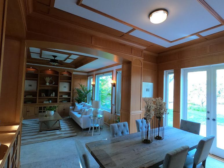 Spacious dining room with wooden paneling, a long table, and a living room visible through an archway.