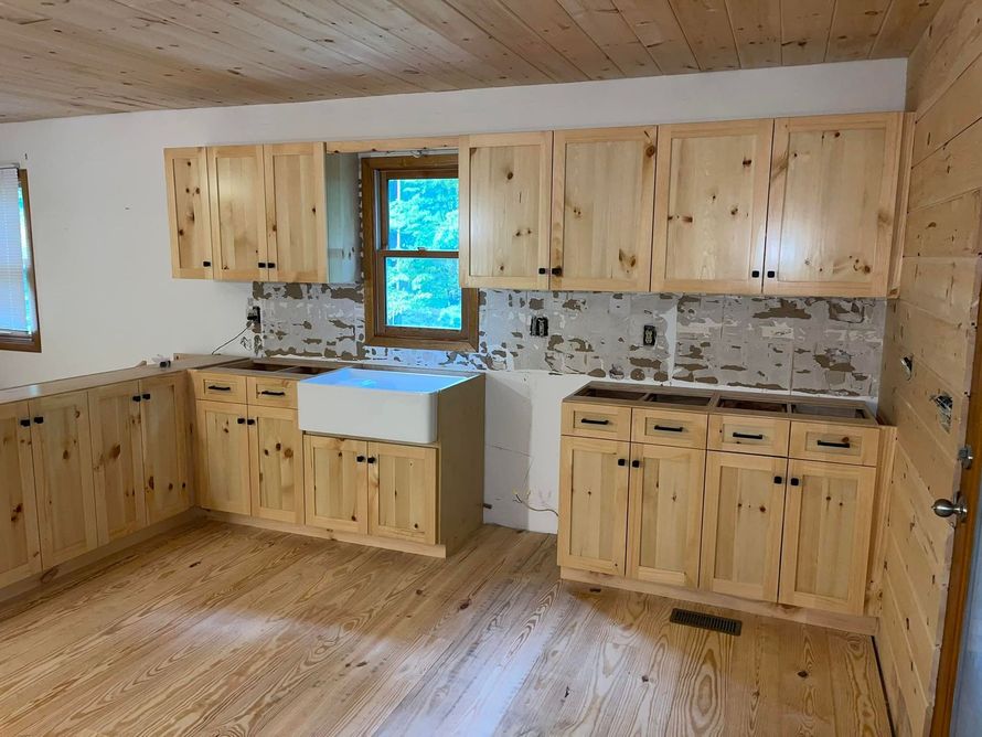 Kitchen with light wood cabinets, flooring and ceiling. A white farmhouse sink is visible. Backsplash tiles are partially.