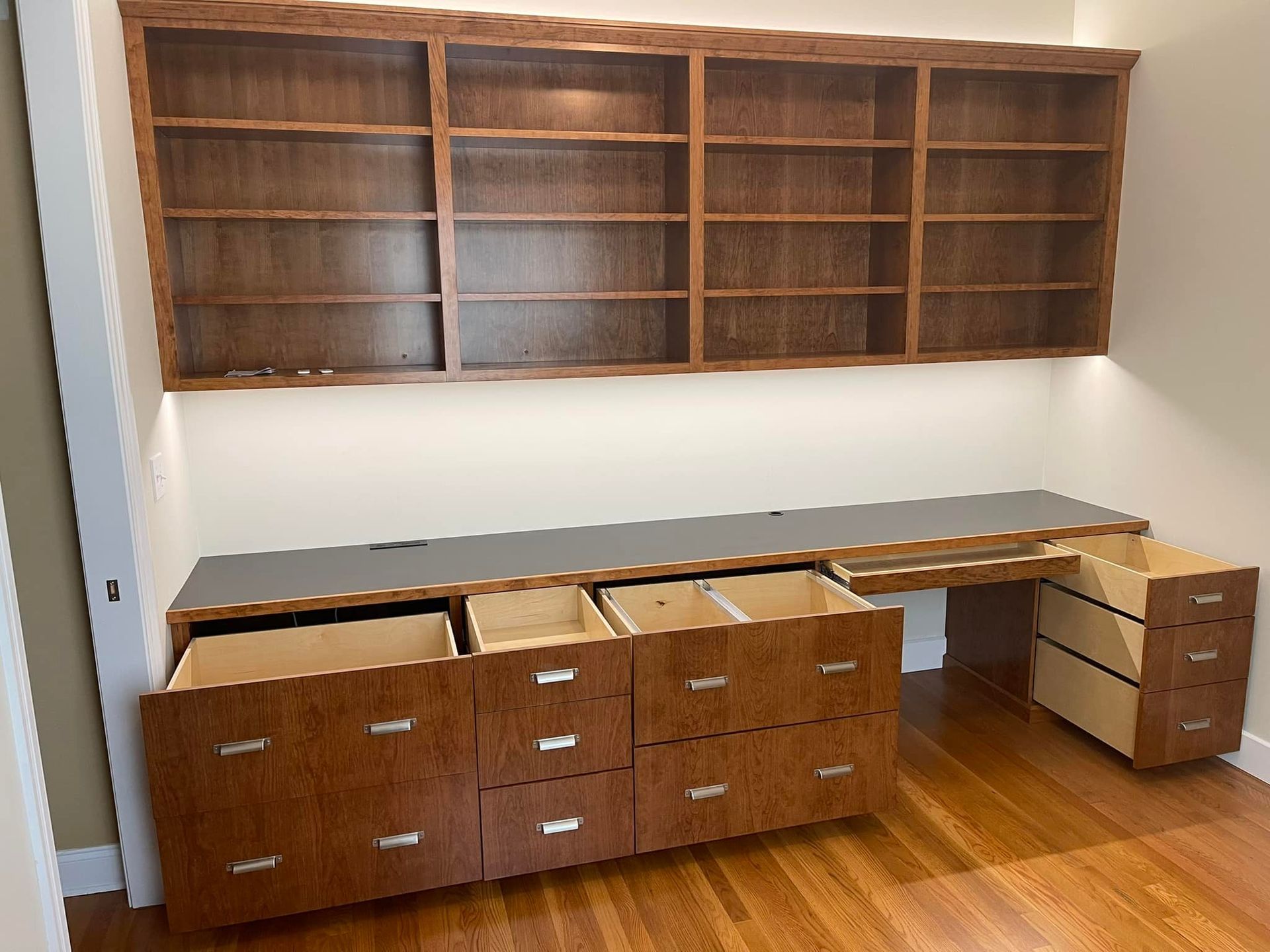 Built-in wooden desk and shelving unit. Dark brown wood, drawers open, set against a light-colored wall.