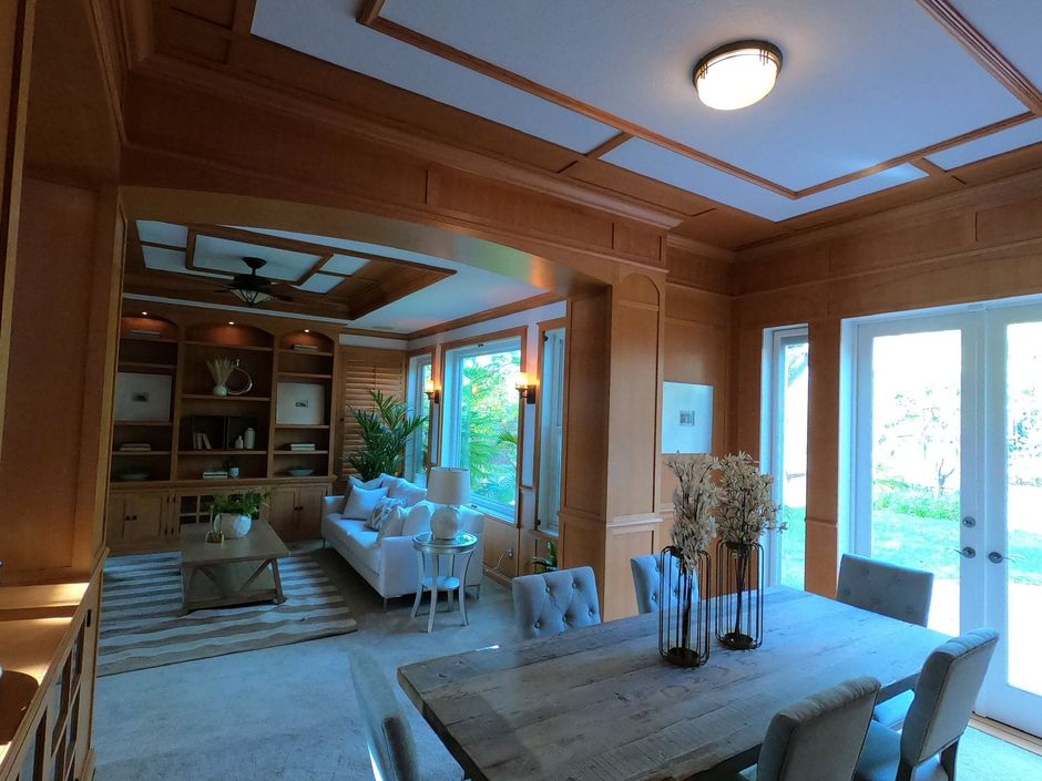 Wood-paneled room with a dining area and living room. A table and chairs are in front of French doors.