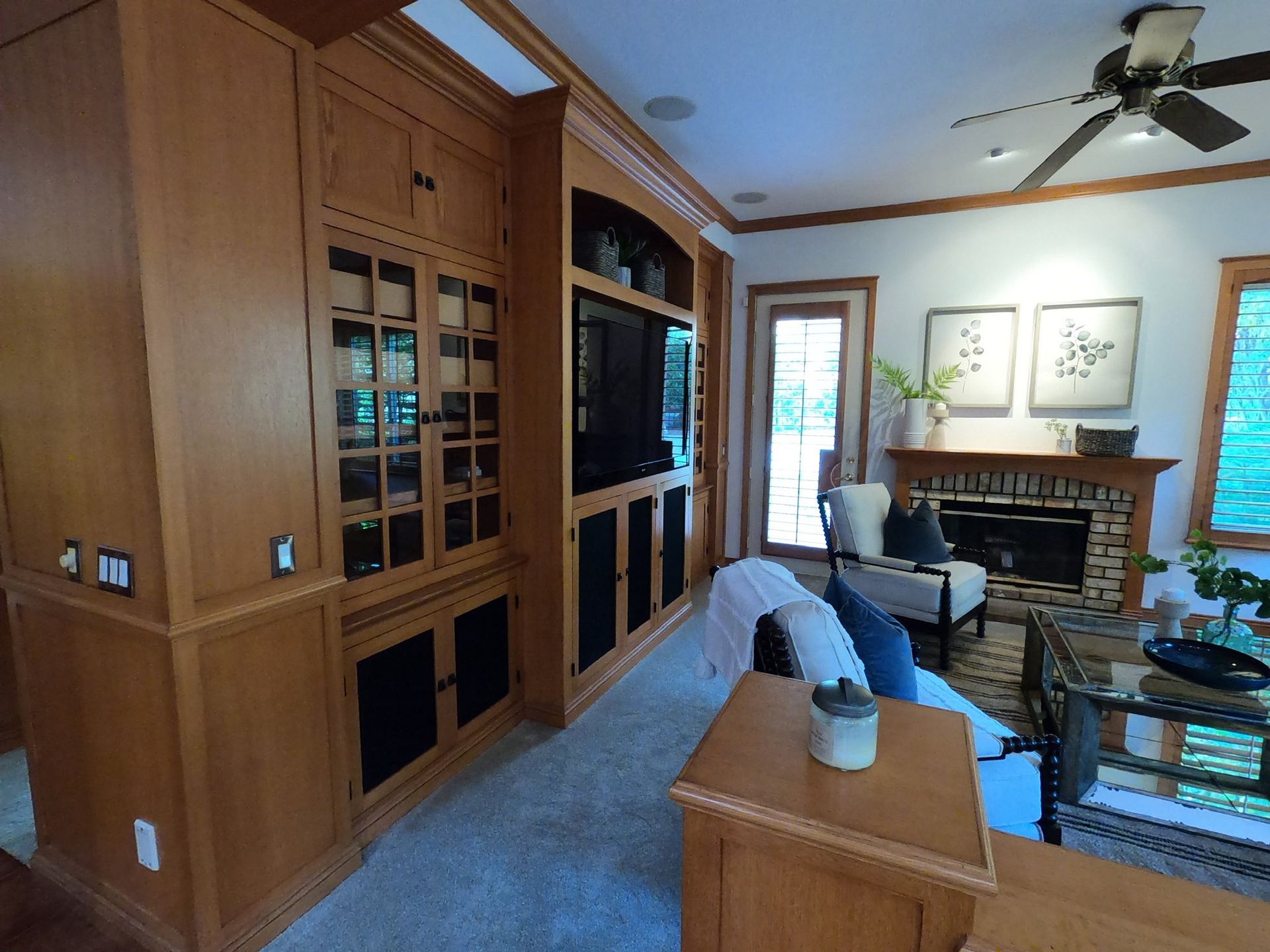 Wooden-paneled dining room with table and chairs. Living room visible through an archway, with windows and a sofa.