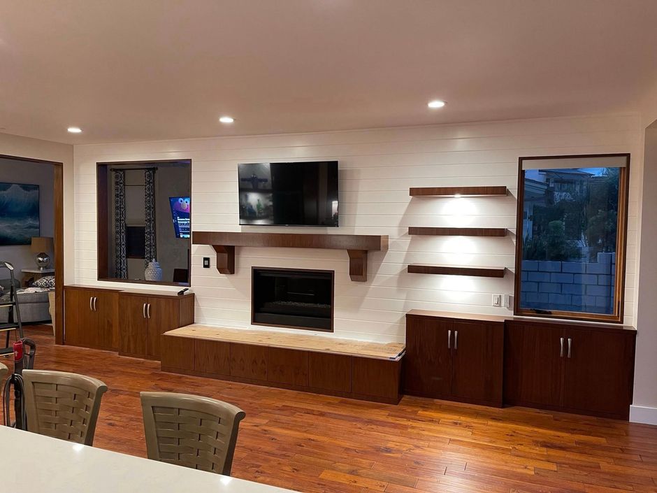 Living room with fireplace, TV, and built-in wooden cabinets against a white brick wall.
